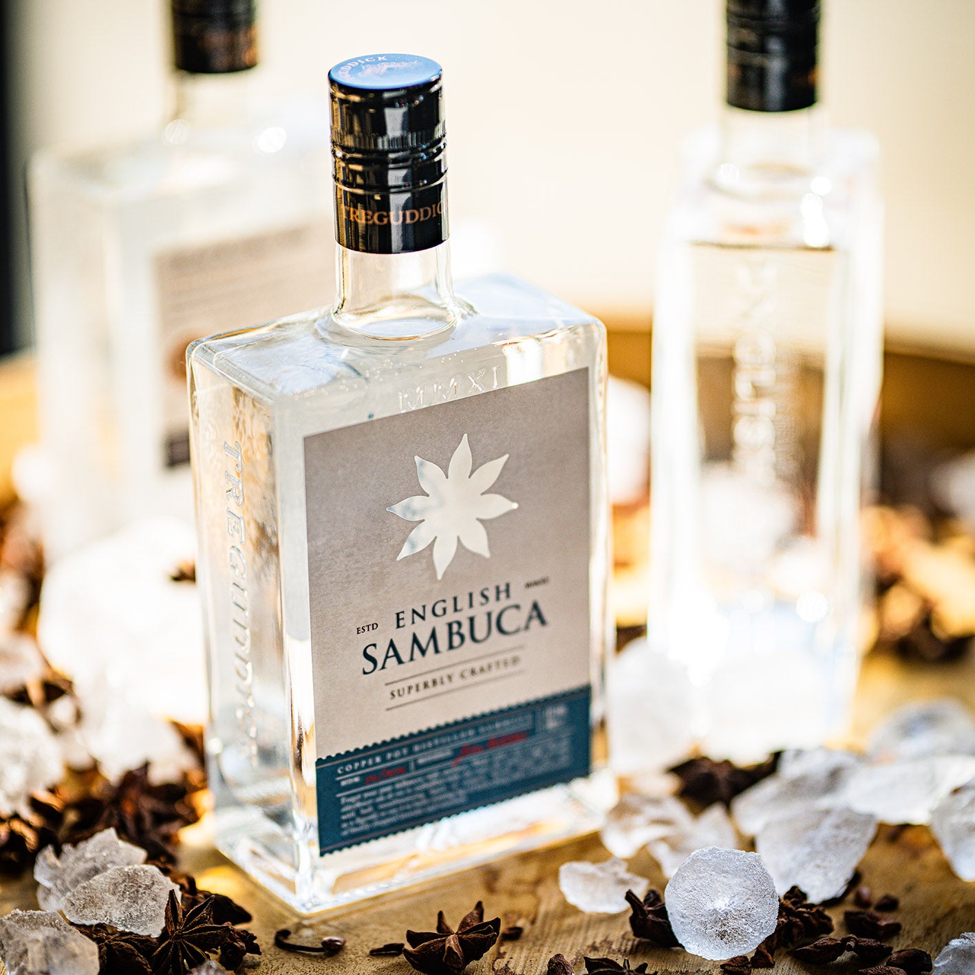 Bottle of The English Sambuca with star anise and ice cubes on a wooden surface.