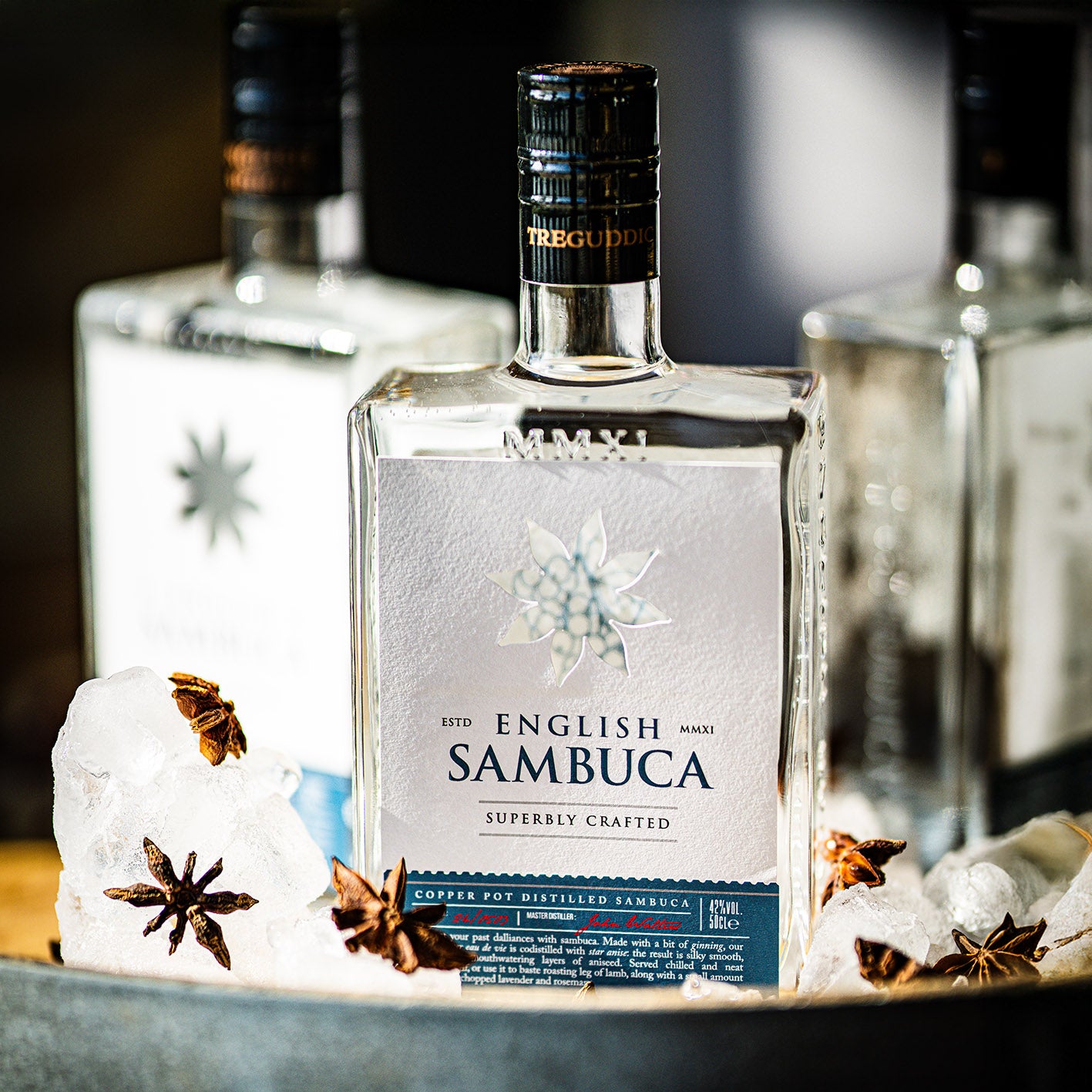 Bottle of English Sambuca with star anise and ice cubes on a dark surface
