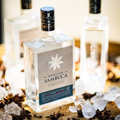 Bottle of The English Sambuca with star anise and ice cubes on a wooden surface.